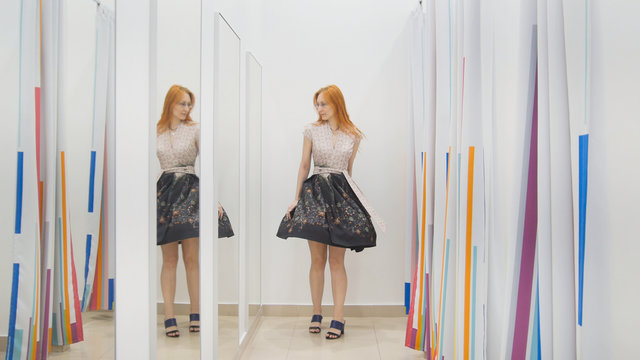 Young woman trying dress near mirror in fitting room - shopping concept