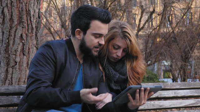 relaxed couple on a bench at the park playing with the tablet