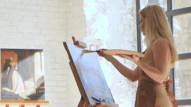 Woman artist paints on canvas broad brush and holds palette