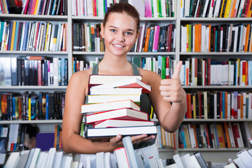 teenager girl holding a stack of books in bookstore