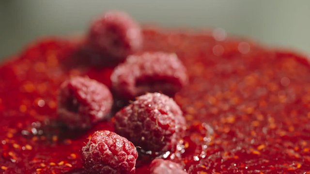 Tilt up macro shot of putting fresh raspberries on top of cake covered with jam