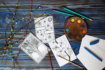 Many postcard in doodling style with drawn picture, pencils and brushes and ceramic plate in form of artistic palette on wooden blue background. Hand drawn, creativity. Top view. Place for inscription