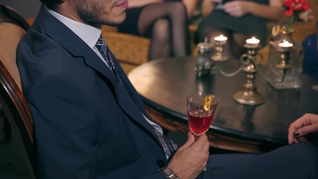 Young businessman sipping his cocktail while listening to his interlocutor