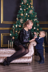 Portrait of happy mother and adorable baby celebrate Christmas. New Year's holidays. Toddler with mom in the festively decorated room with Christmas tree and decorations.