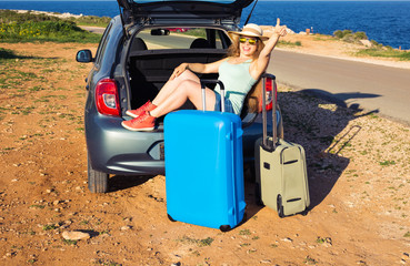 Travel, summer holidays and vacation concept - Young woman with suitcases on car trip. She is sitting in car back and gesture thumbs up.