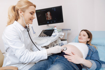 Lively obstetrician using stethoscope for checkup in the hospital