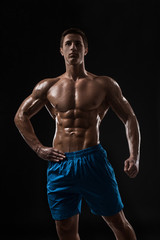 Fototapeta premium Muscular and fit young bodybuilder fitness male model posing over black background.