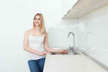 Beautiful young woman holds a glass with water on kitchen