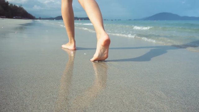 Woman walking on beach barefoot at sunset. Female strolling on sand near sea.