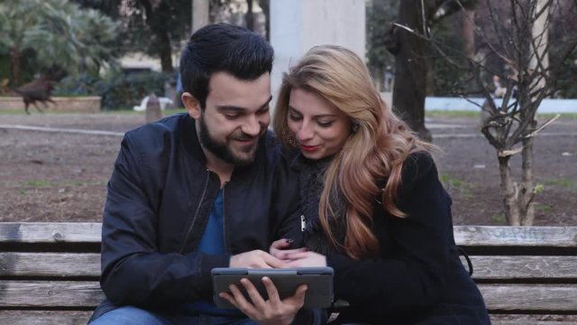 Portrait of Happy,smiling couple on the bench looking at photos on the tablet