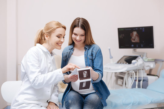 Amused young obstetrician enjoying conversation with patient at work