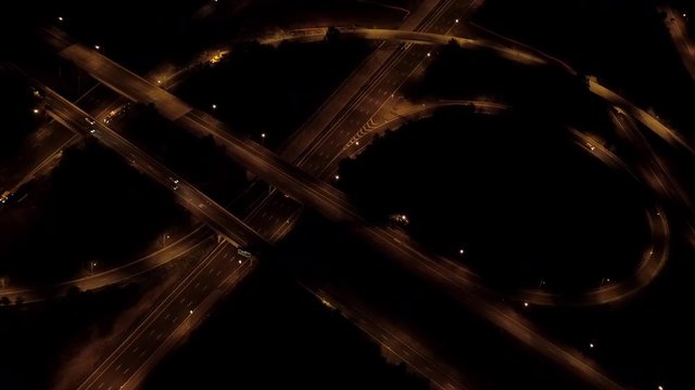 AERIAL HELI SHOT Flying above two level stack interchange road junction on expressway highway with on-ramp and off-ramp for traffic to pass through. Cars, trucks & trailers traveling along the freeway