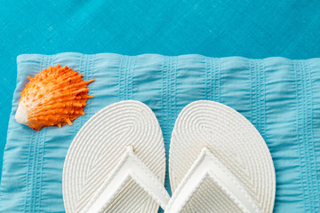White flip flop near seashell on blue background. Top view.