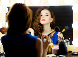 portrait of beautiful young woman holding brush and looking at herself in the mirror