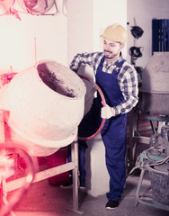 Young smiling guy using concrete mixer at workshop