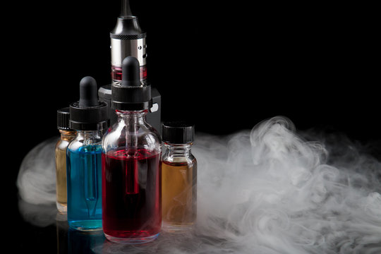 Electronic cigarette and e-liquids on black background with smoke