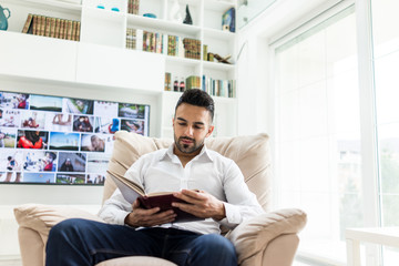 Young confident man reading book at modern home