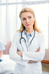 portrait of pensive doctor with stethoscope standing with crossed arms in hospital