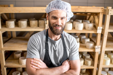 Handsome cheese maker checking the aging process of the goat cheese standing at the small cellar