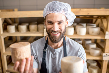 Handsome cheese maker checking the aging process of the goat cheese standing at the small cellar
