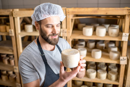Handsome cheese maker checking the aging process of the goat cheese standing at the small cellar