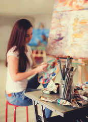 Fototapeta premium Female Artist Working On Painting In Studio. Background image, selective focus on foreground
