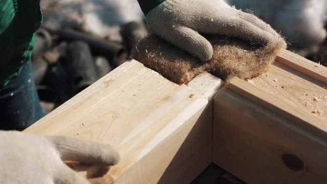 Close up hands in work gloves connect two wooden blocks with oakum in between in winter