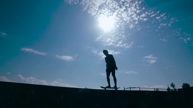 Young boy silhouette is skating on the edge of the fence. HD.