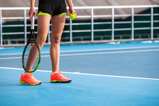 Legs of young girl in a closed tennis court with ball and racket
