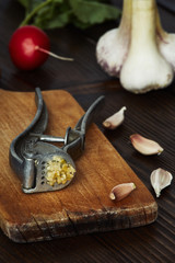 Garlic press on a cutting board on a wooden table. Closeup vertical image.