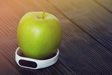 Green apple with fitness tracker on a wooden table.
