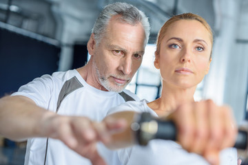 portrait of sportswoman and senior trainer training with dumbbells in sports center