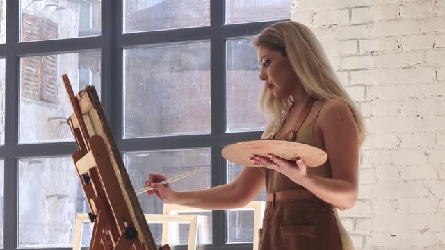 Woman artist inspired paints picture on canvas mounted on easel