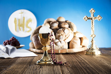 First Holy communion. Catholic theme. Crucifix, chalice, bible, bread on rustic wooden table and blue background.