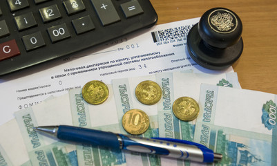  На столе в кабинете лежит налоговая декларация, печать калькулятор на котором лежат деньги –купюры монеты РФ  - obrazy, fototapety, plakaty