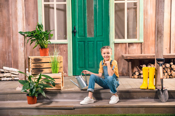 Adorable smiling little girl sitting on porch with watering can © LIGHTFIELD STUDIOS