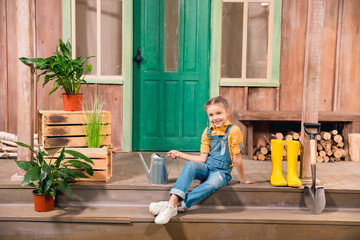 Adorable smiling little girl sitting on porch with watering can © LIGHTFIELD STUDIOS