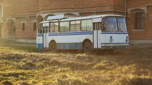 Old vintage white blue soviet union ussr relic bus in sunny summer day in field in front of yellow orange brick wall, Steady cam, slow mo shot