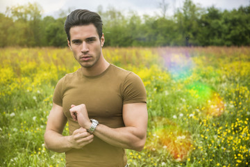 Naklejka na ściany i meble Attractive, fit young man relaxing standing on lawn in the countryside among grass, looking at camera, smiling