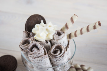 Roll of ice cream with crushed chocolate cookies. Fresh fried ice cream, ice roll on a light wooden background