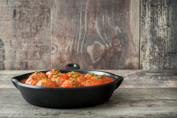 Meatballs with tomato sauce in iron frying pan on wooden table
