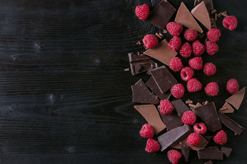 Dark and milk chopping chocolate and chips shavings chopping chocolate with fresh raspberries heap over black burnt wooden background. Top view with space. Chocolate dessert concept