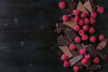 Gartenposter Dark and milk chopping chocolate and chips shavings chopping chocolate with fresh raspberries heap over black burnt wooden background. Top view with space. Chocolate dessert concept © Natasha Breen