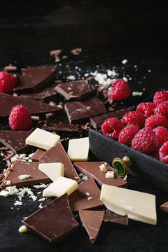 Variety of dark, milk and white chopping chocolate with fresh raspberries in black wood box over black burnt wooden background. Close up. Chocolate dessert concept