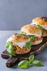 Homemade mini burgers with pulled chicken, basil, mozzarella cheese and yogurt sauce on wooden serving board over gray texture background. Healthy fast food concept