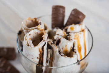 Roll of ice cream with crushed caramel candy. Fresh fried ice cream, ice roll on a light wooden background. Ice cream with caramel