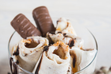 Roll of ice cream with crushed caramel candy. Fresh fried ice cream, ice roll on a light wooden background. Ice cream with caramel