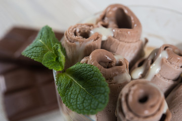 Roll of chocolate ice cream. Fresh fried ice cream, ice roll on a light wooden background. Ice cream with chocolate and mint