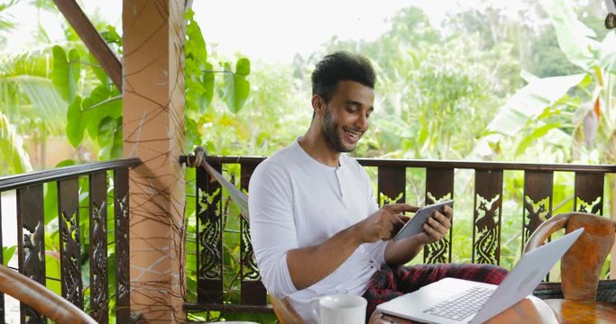 Young Man Using Tablet Computer Laughing On Terrace, Hispanic Guy Chatting Online Slow Motion 60