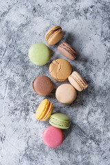 Variety of colorful french sweet dessert macaron macaroons with different fillings served over gray texture background. Top view with space